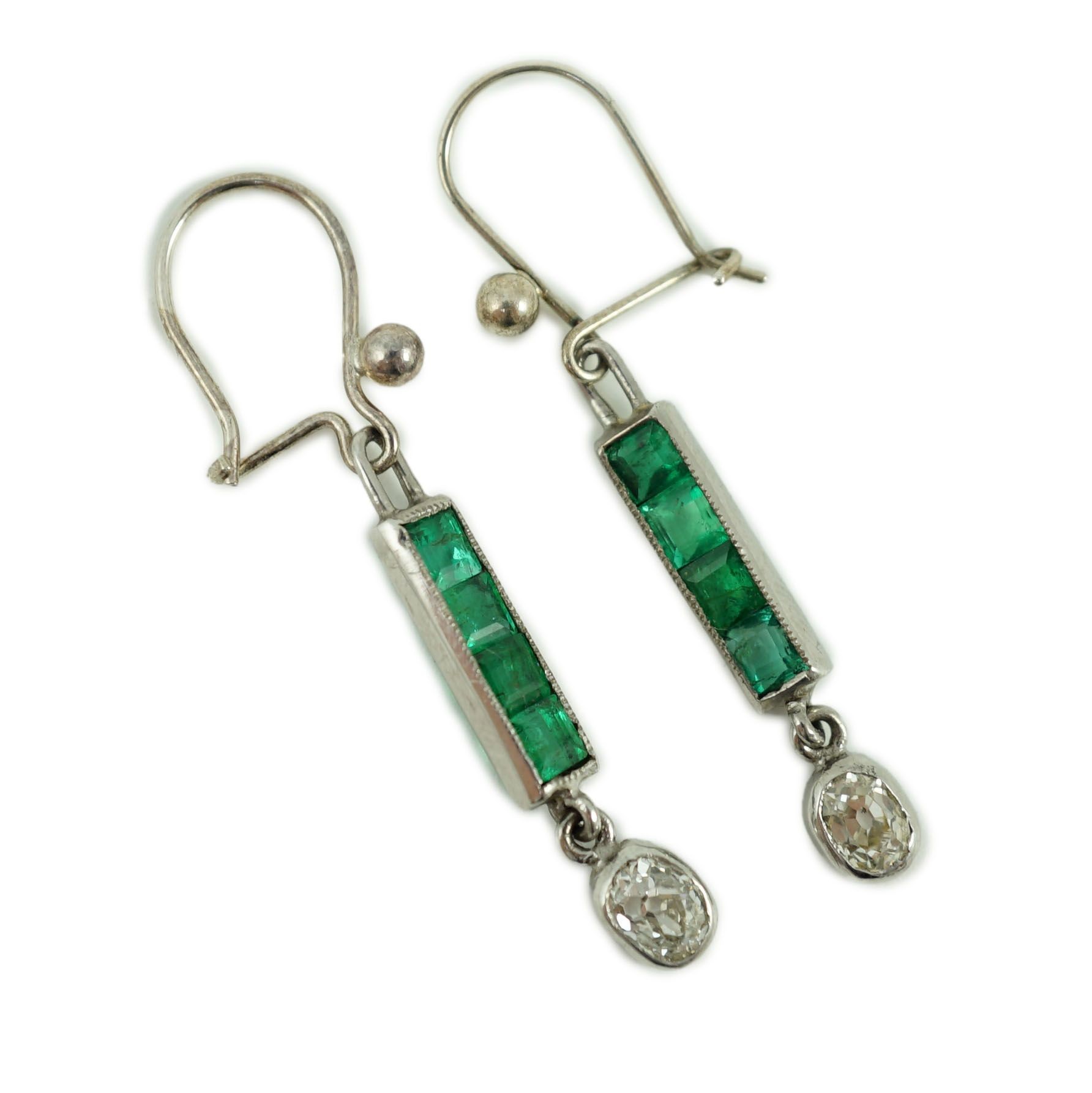 A pair of white gold, four stone emerald and single stone oval cut diamond set drop earrings